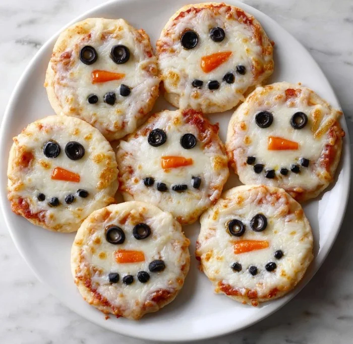 Mini snowman pizzas decorated with toppings for a festive holiday snack.