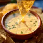 Delicious bowl of Chile con Queso topped with cheese and fresh herbs
