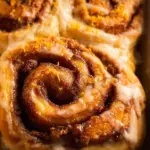 Freshly baked orange cinnamon rolls topped with glaze on a cooling rack