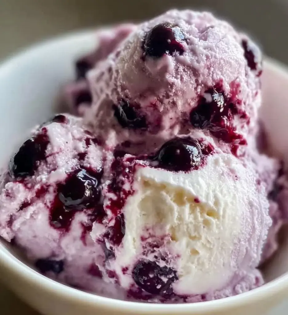 Blueberry cottage cheese ice cream in a bowl with fresh blueberries on top.