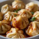 Plate of delicious Chicken Momo Dumplings served with a spicy dipping sauce.