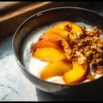 High-protein peach cobbler Greek yogurt bowl topped with fresh peaches and yogurt.